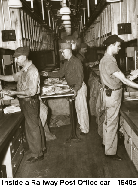 Black and white photo of four men wearing railroad engineer's caps and holstered pistols sorting mail at long counters while standing in a narrow railroad car whose walls are covered with cabinets and cubbyholes.